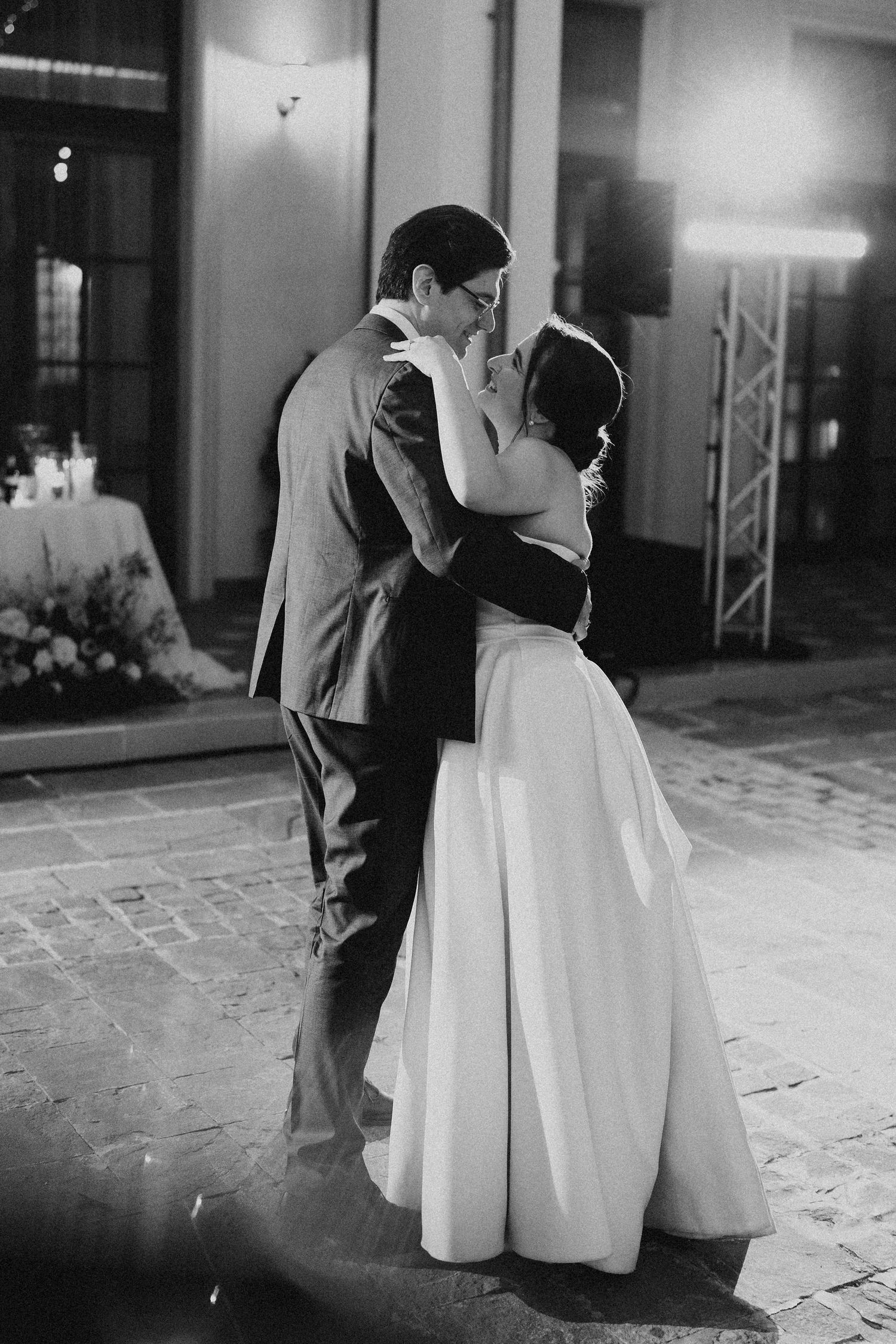Black and white photo of bride and groom sharing first dance kiss at elegant outdoor wedding reception.