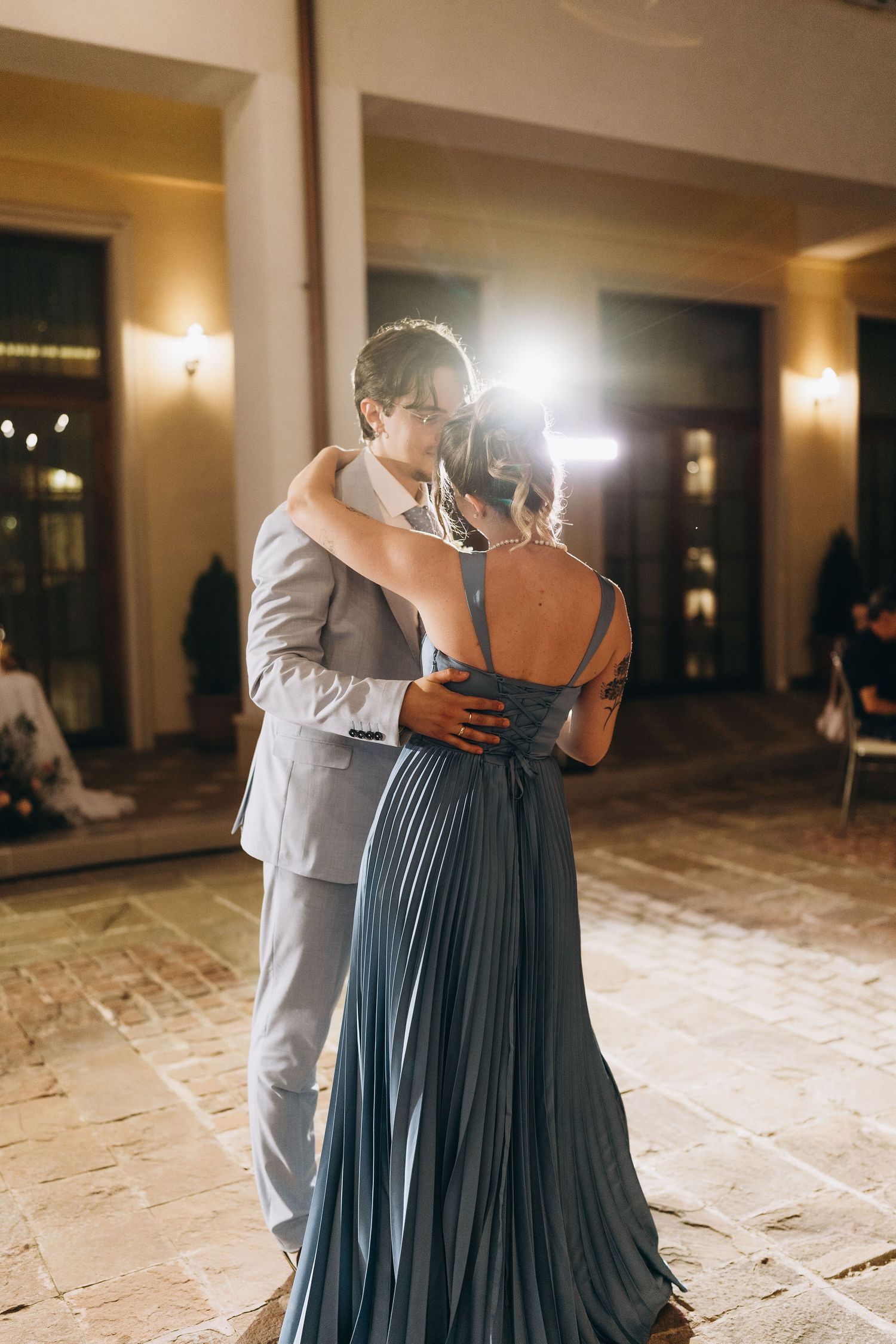 Couple sharing romantic first dance at wedding reception, woman in elegant blue pleated gown, man in gray suit.