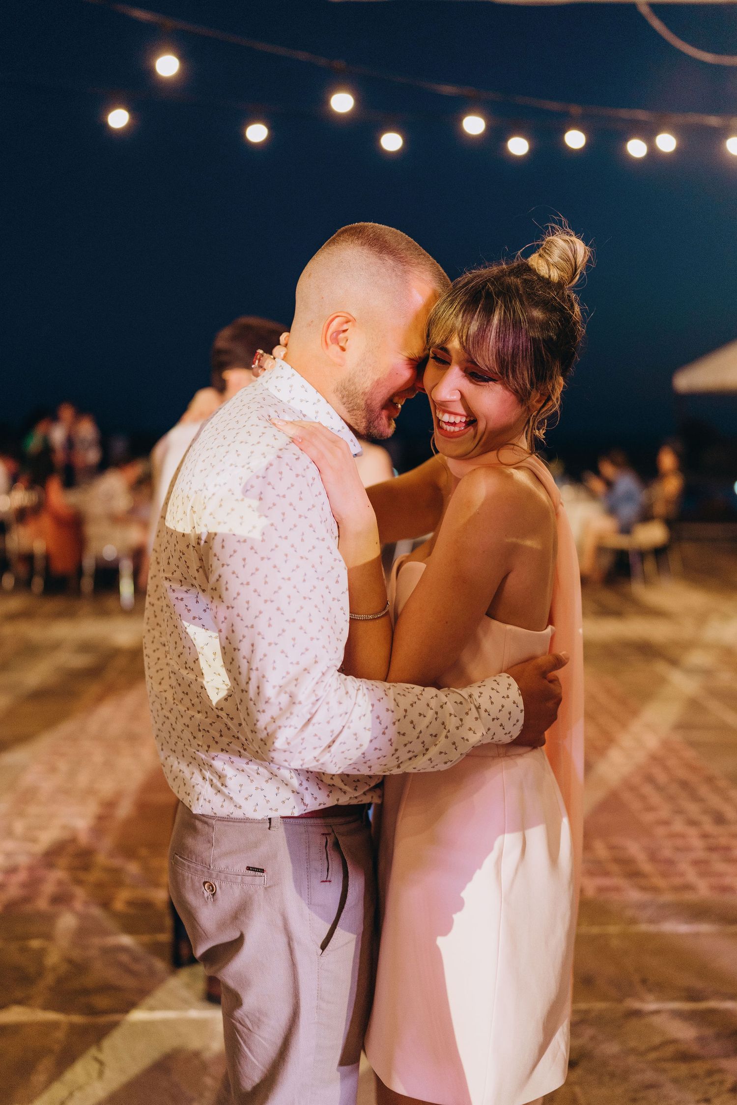 Couple sharing a romantic dance under string lights at an outdoor evening wedding reception.