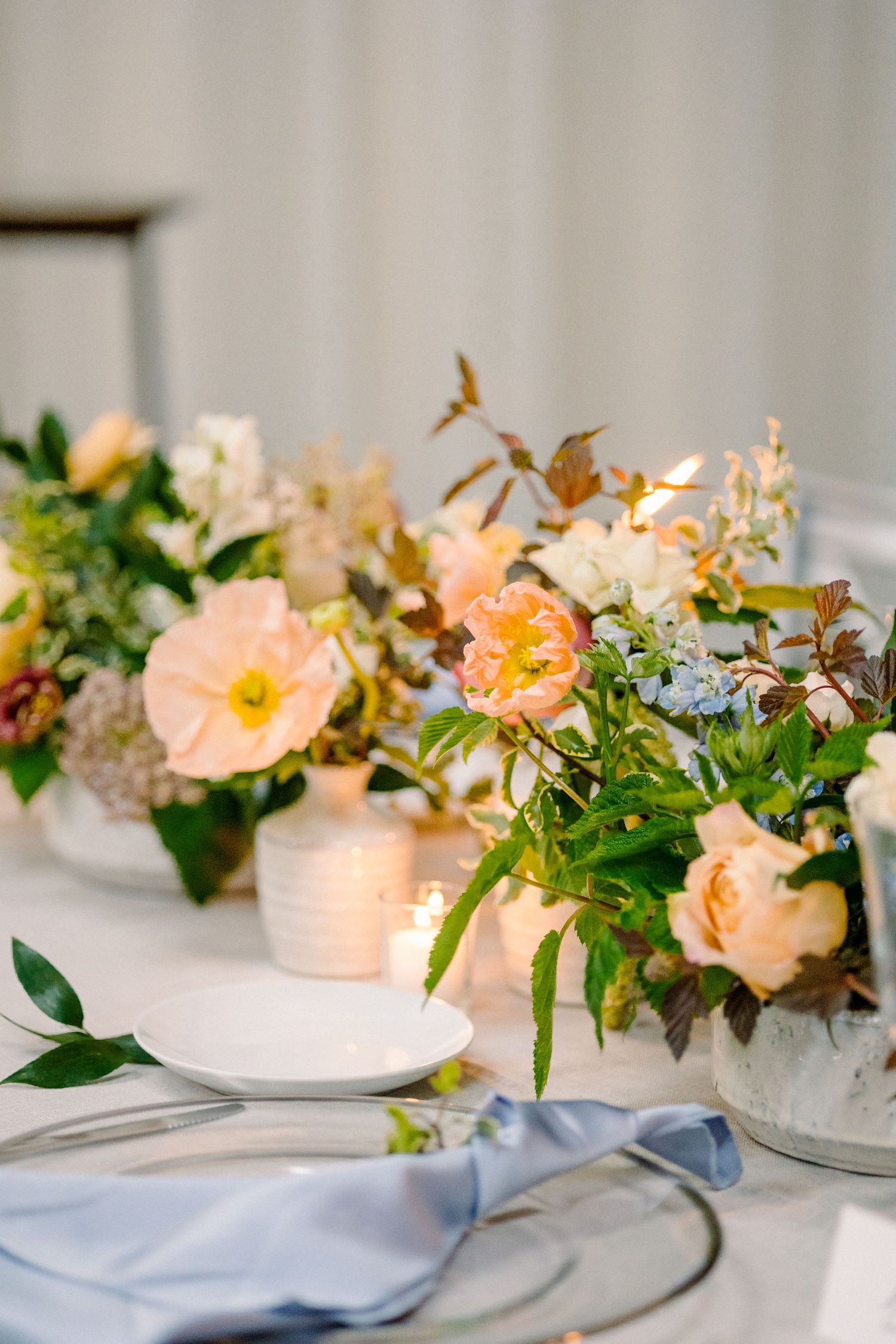 Elegant wedding reception table with white floral centerpiece, candles, balloon, and dark brown linen in a bright banquet hall.
