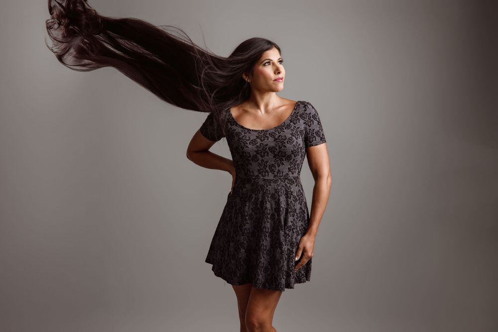 Miami personal branding portrait of a woman in a gray patterned dress with her long dark hair flowing against a studio background.