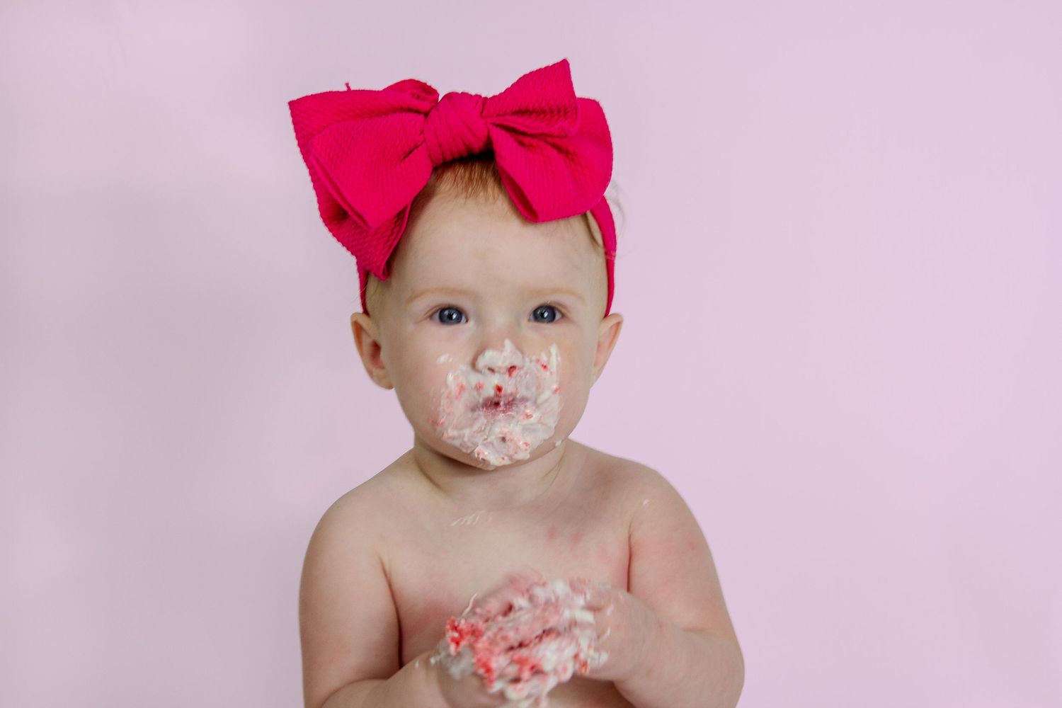 a baby eating cake on a pink background during a cake smash session in Northeast Arkansas
