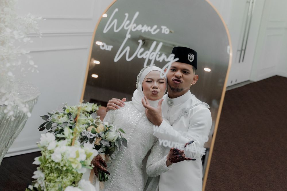 Muslim couple posing together at their wedding in front of a decorative mirror sign reading Welcome to Our Wedding.