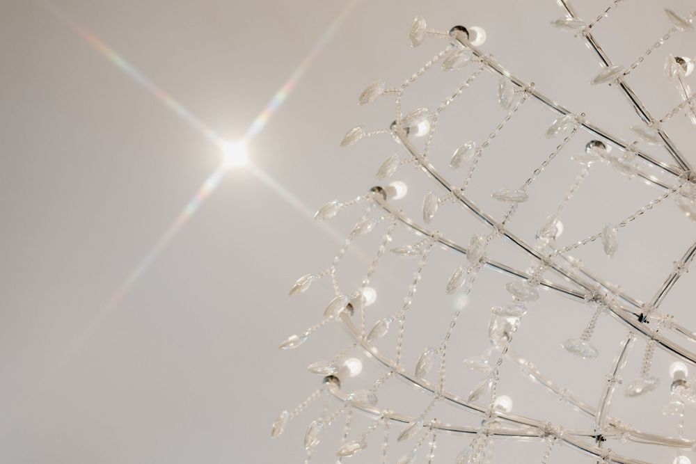 Crystal chandelier branches with glass beads reflecting bright star-shaped light against a white ceiling.