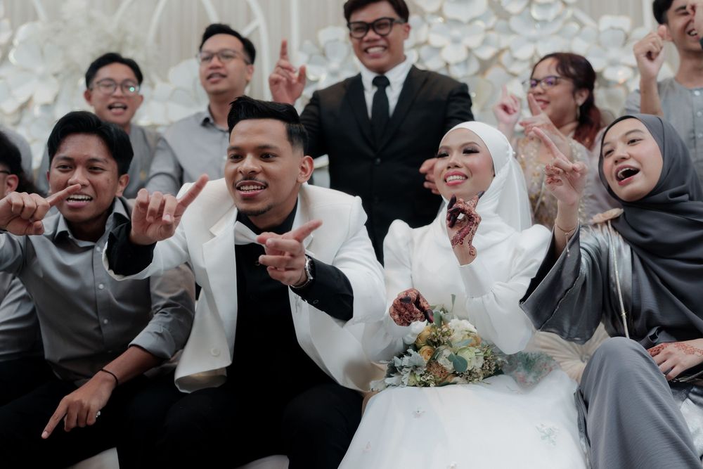 Muslim bride and groom celebrate wedding with joyful guests in elegant white floral venue.