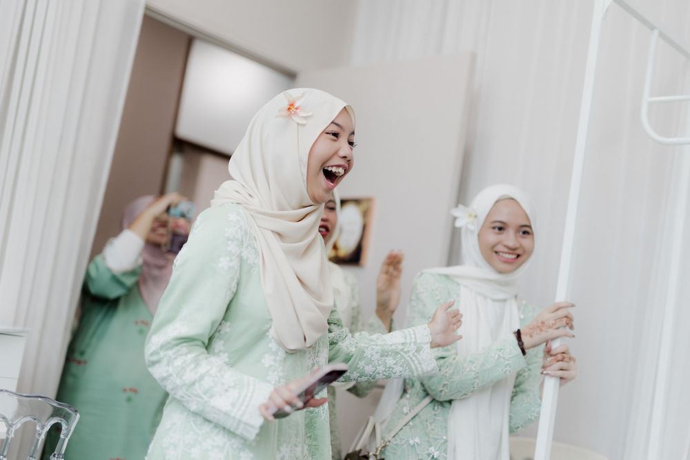 Two women in hijabs laughing joyfully at a celebration, wearing elegant mint green and white traditional attire.