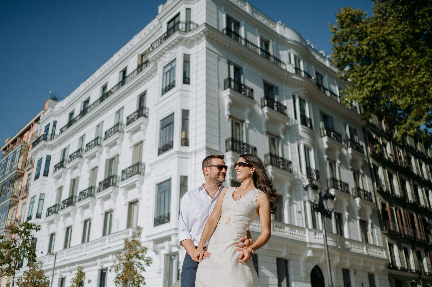 Couple posing romantically in front of a grand white European building on a sunny day.