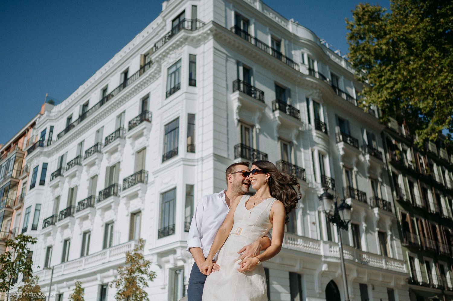 Couple sharing a romantic kiss in front of a elegant white European building on a sunny day.