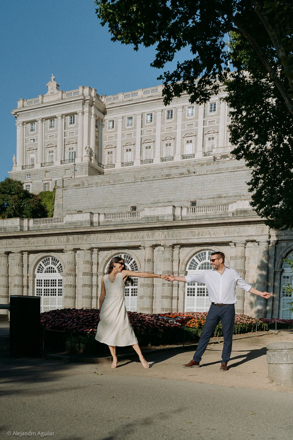Couple dancing playfully in front of the Royal Palace of Madrid on a sunny day.