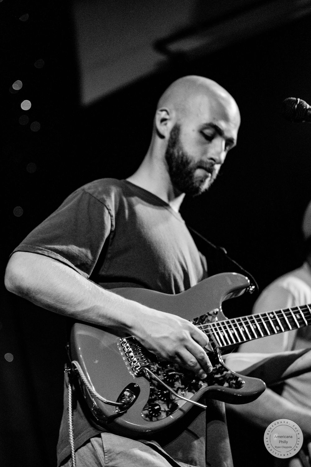 Bald bearded man playing electric guitar on stage in black and white concert photography.