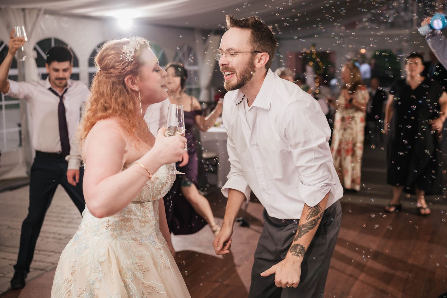 Bride dancing alone with her eyes closed, holding a bubble gun overhead as bubbles fill the reception tent around her.