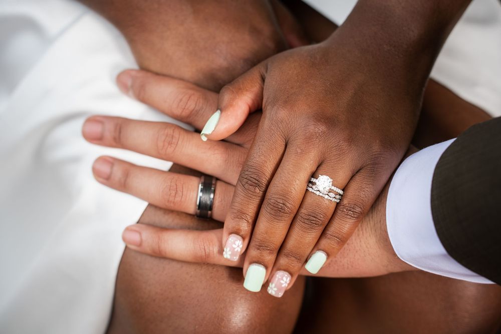 Bride and groom hands showing wedding rings with manicured nails.