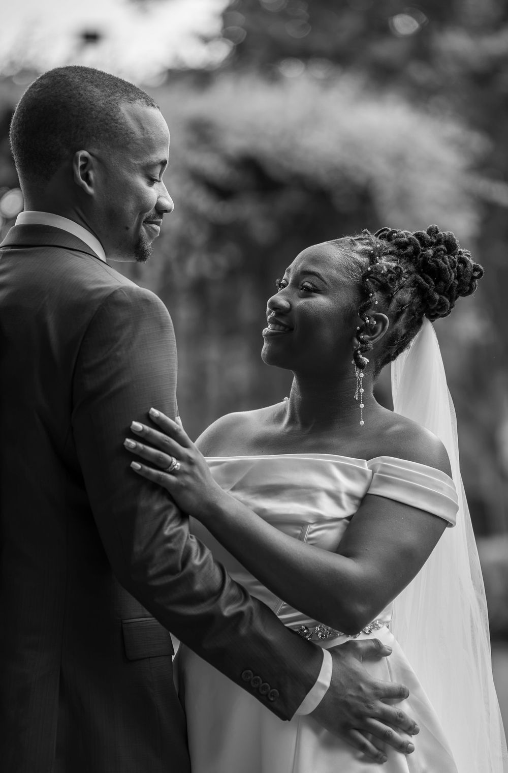 Black and white photo of a bride and groom sharing an intimate moment, smiling at each other during their wedding.