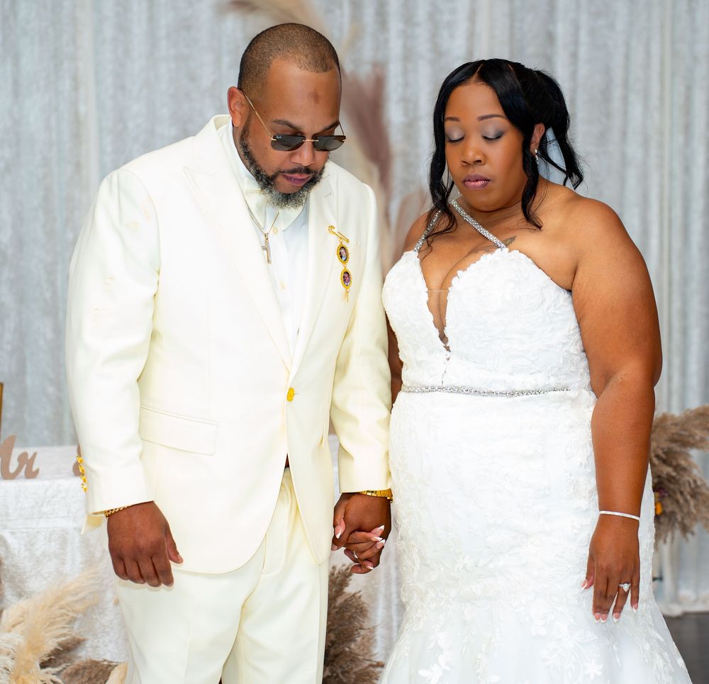 Bride and groom holding hands in matching white wedding attire at an elegant indoor ceremony.