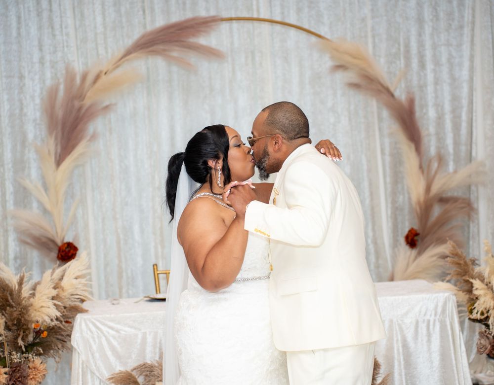 Newlyweds sharing a kiss under a circular pampas grass arch at their wedding reception.