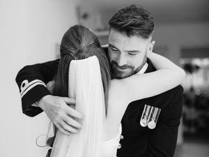 Emotional black and white photo of groom in military uniform embracing bride on wedding day.
