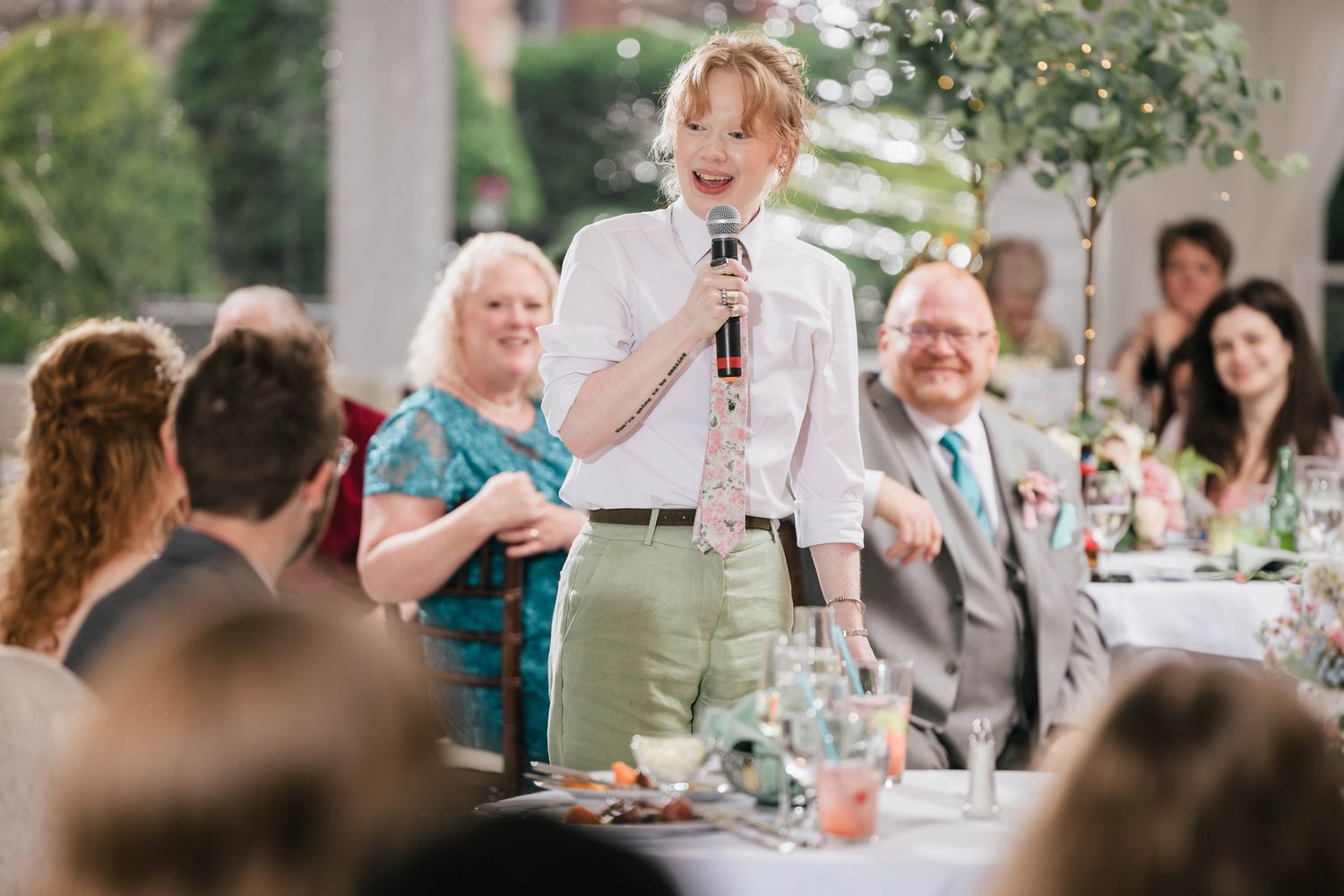 Maid of honor mid-laugh during her speech, guests smiling and laughing behind her.