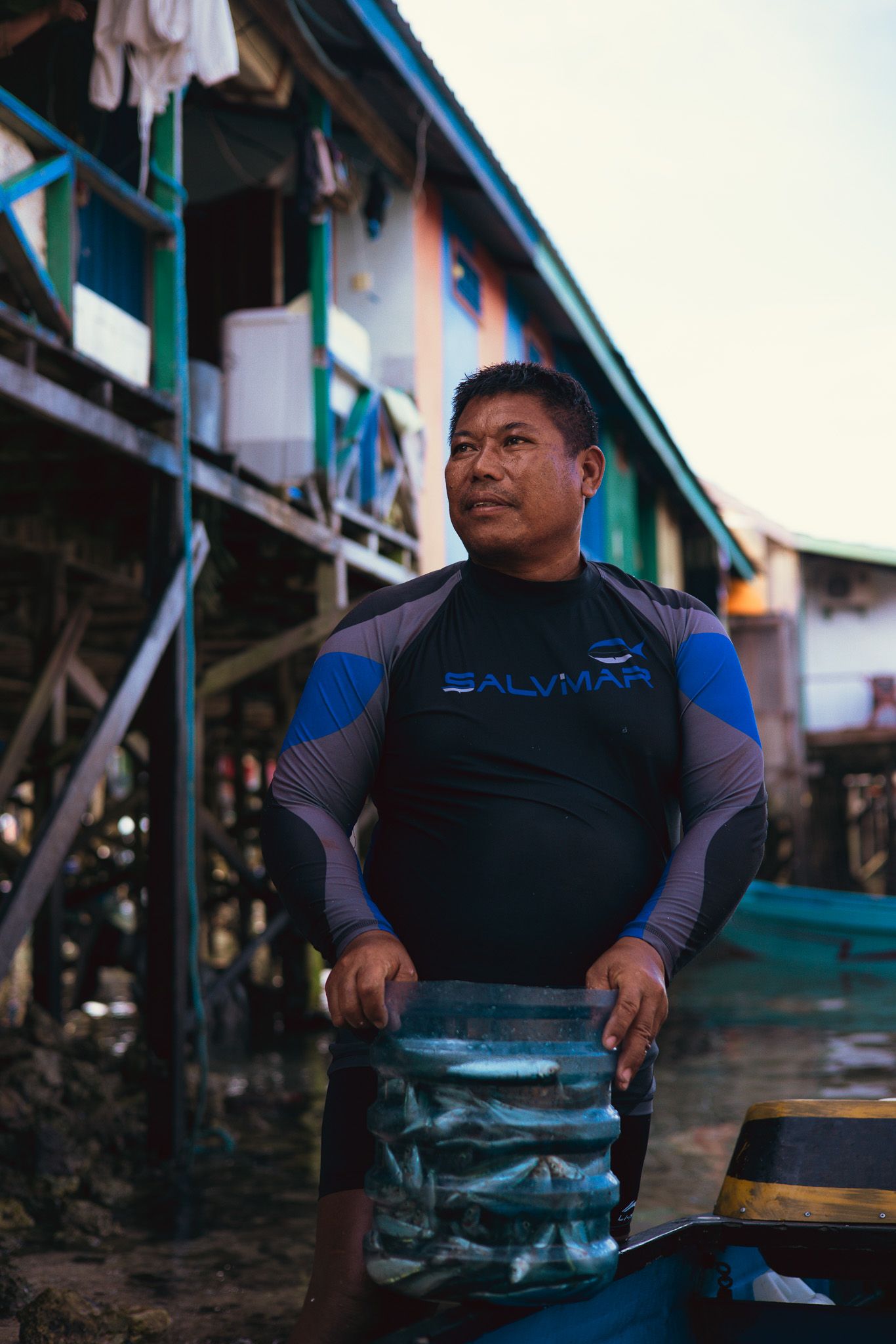 Bajau fisherman standing with his catch beside a coastal village.
