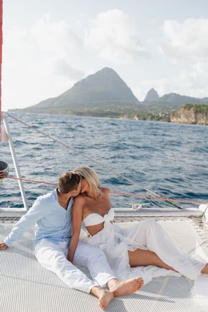 Romantic couple kissing on a catamaran sailboat deck with stunning ocean and mountain views.