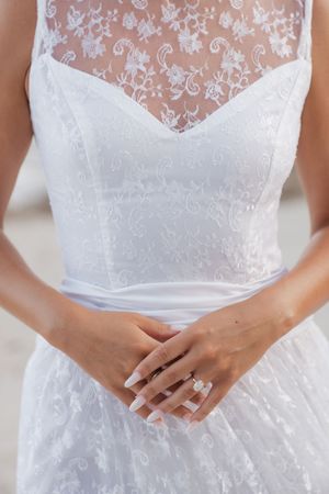 Close-up of bride in white lace wedding gown with floral embroidery and diamond engagement ring.