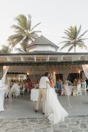 Bride and groom share first dance at tropical outdoor wedding reception with palm trees and string lights.