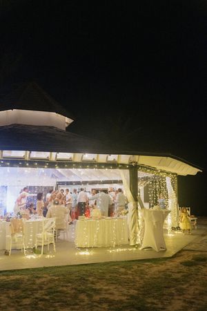 Outdoor wedding reception pavilion glowing with fairy lights at night with guests celebrating inside.