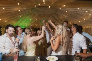 Wedding guests raising glasses in a toast under a tented reception venue with warm string lights.