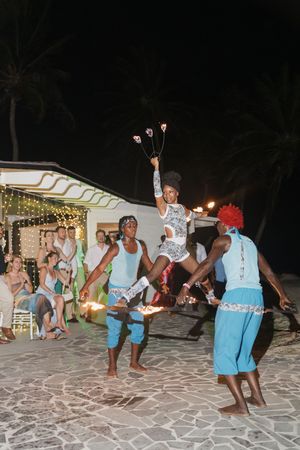 Traditional fire dancers performing at outdoor tropical wedding reception at night for seated guests.