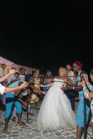 Bride in white gown laughs joyfully while dancing with guests at outdoor nighttime wedding celebration.
