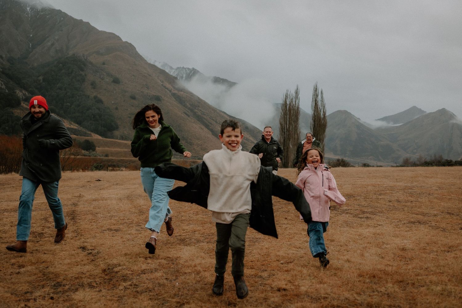 Family joyfully running through a scenic mountain valley with misty peaks and golden grasslands in the background.