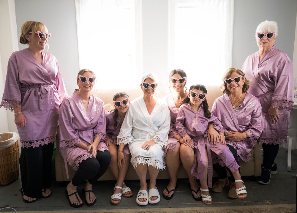 Bride and bridesmaids wearing matching purple robes and heart sunglasses posing together before wedding.