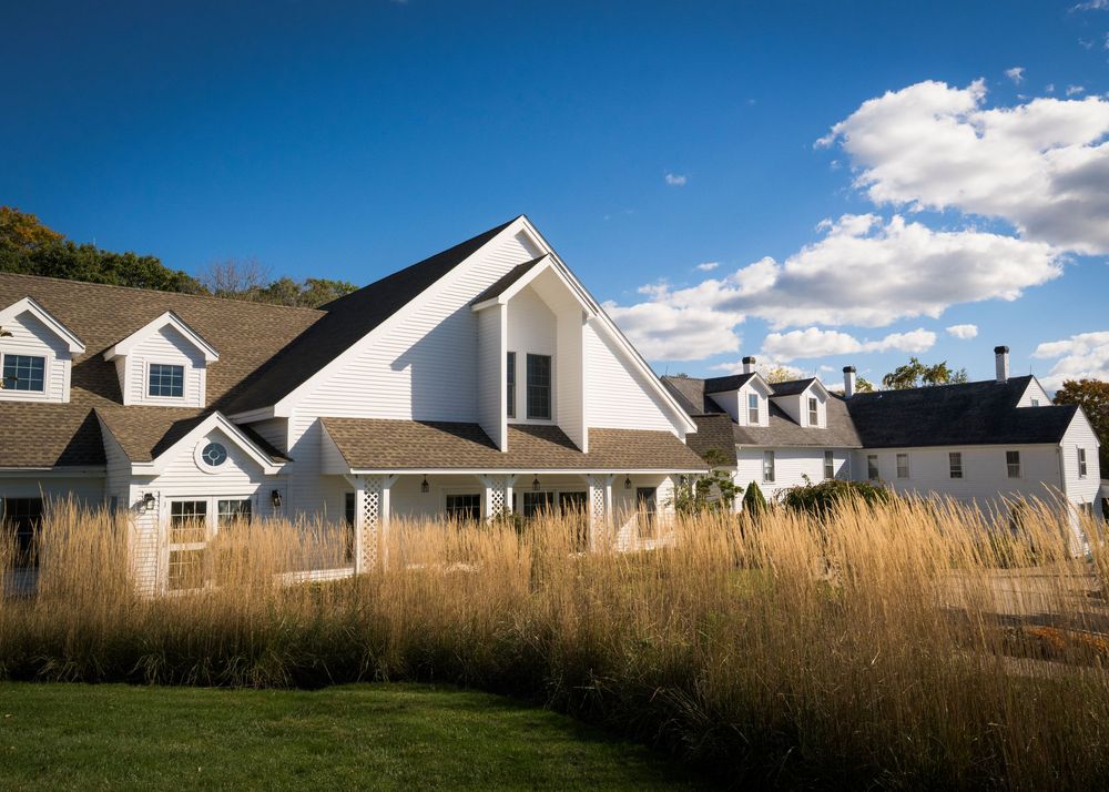 White farmhouse-style wedding venue surrounded by tall golden grasses under a bright blue sky.