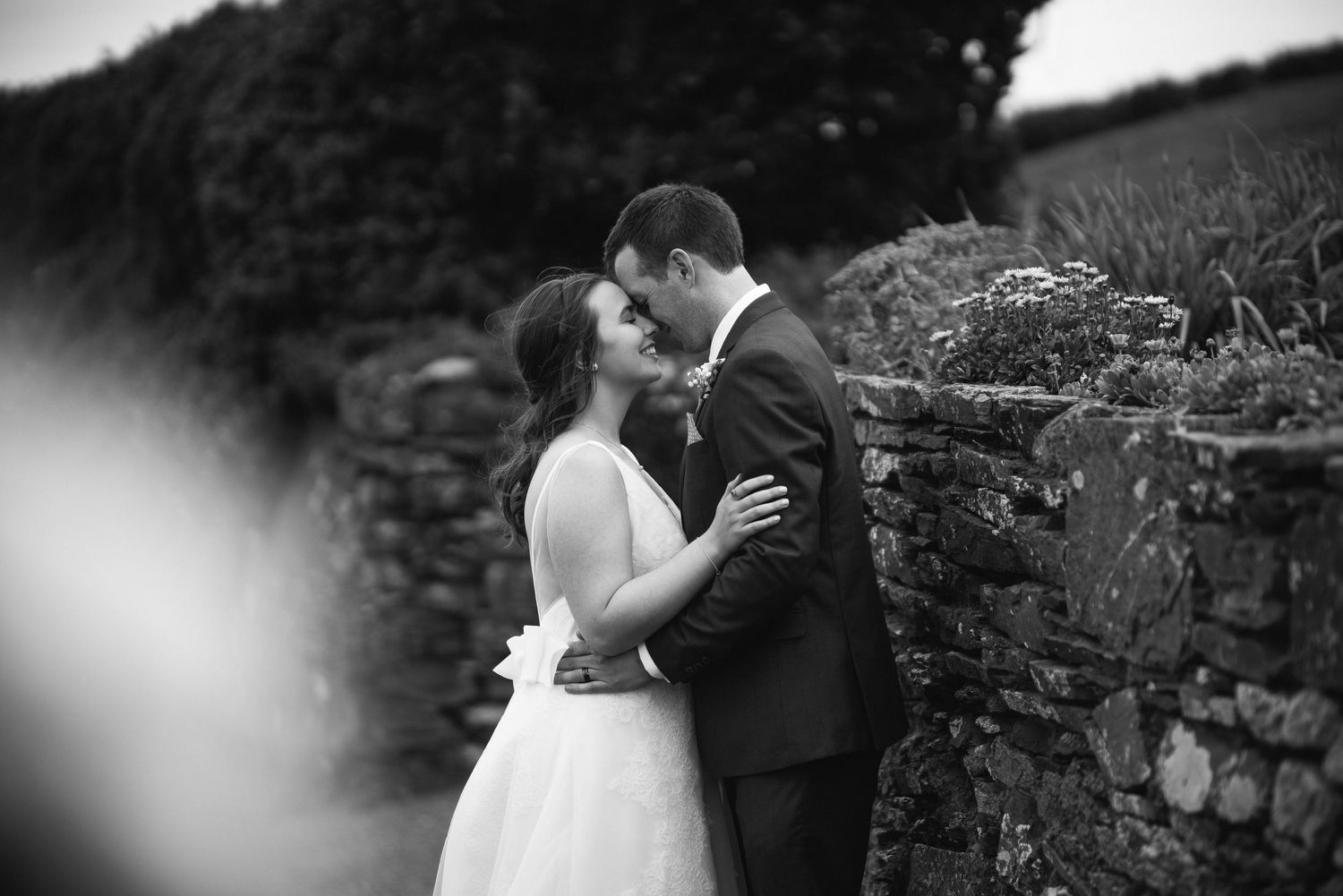 Black and white portrait of bride and groom kissing against a rustic stone wall