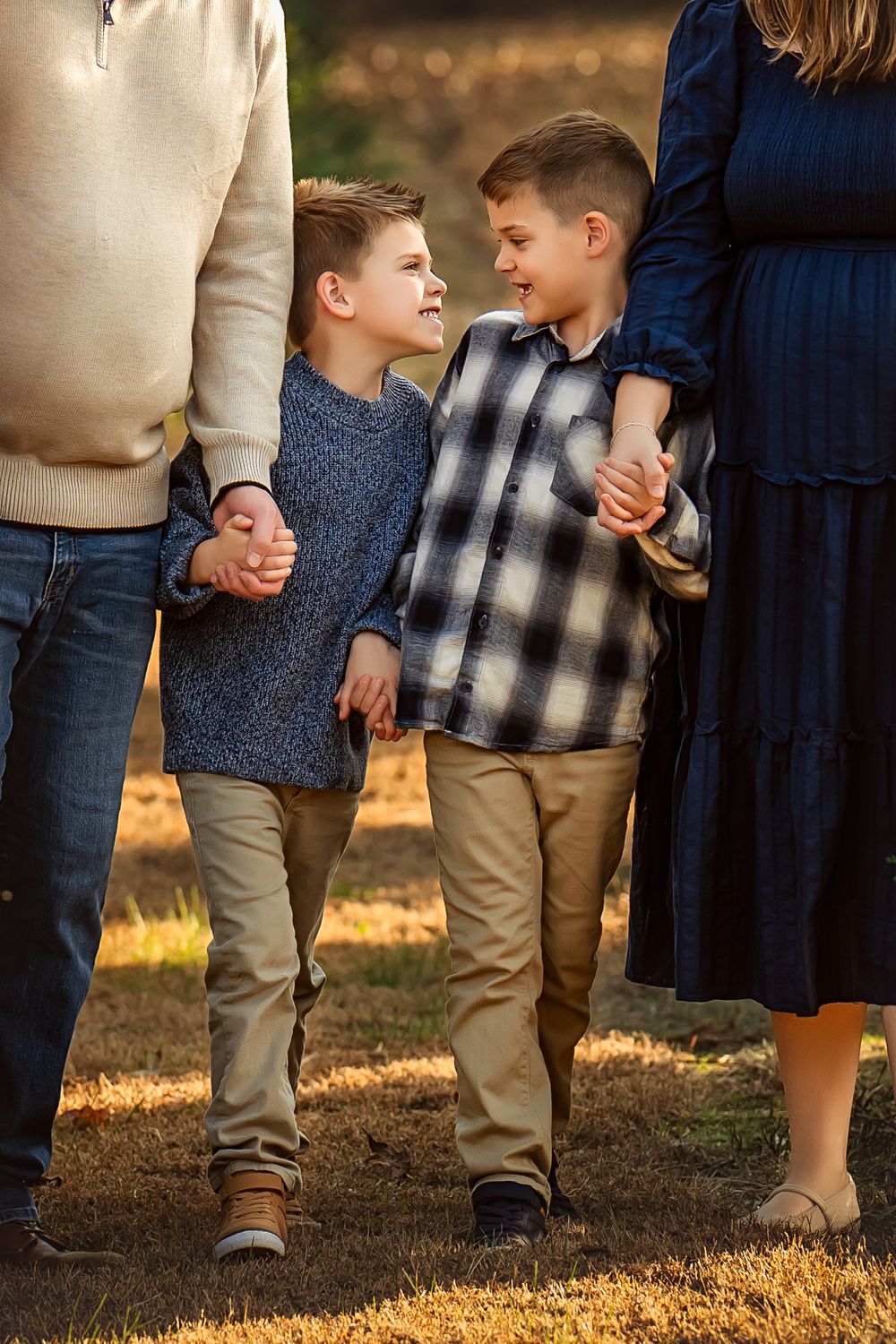 Two young brothers holding hands with parents during a warm golden hour family photo session outdoors.