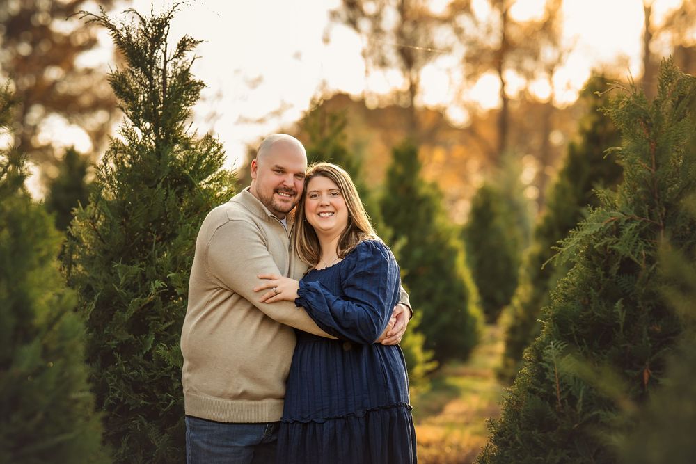 Couple embracing among green Christmas trees at golden hour in a festive tree farm outdoor photo session.