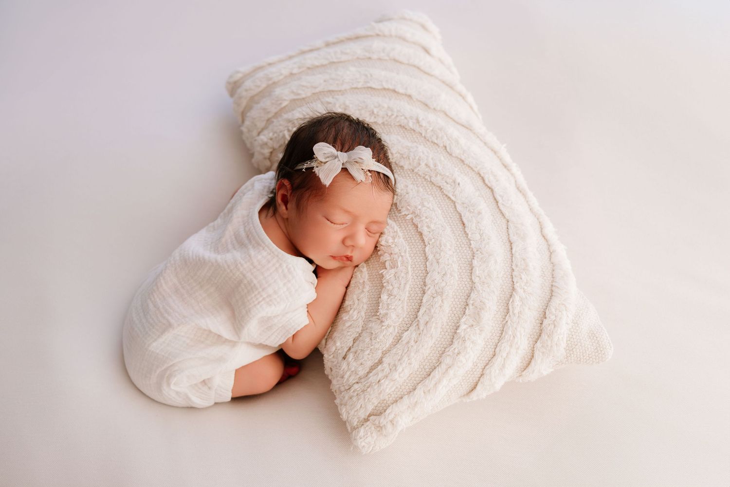 Smiling pregnant woman in white lace dress holding belly beside pampas grass decor.