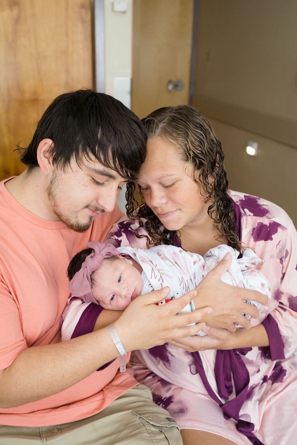 New parents tenderly hold their swaddled newborn baby in a hospital room, sharing a precious first family moment.