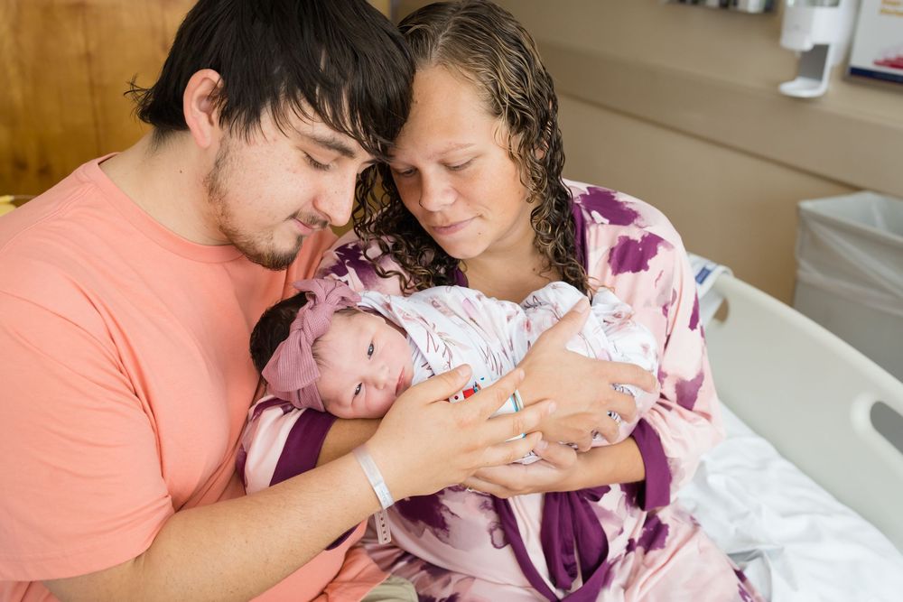 New parents lovingly hold their swaddled newborn together in a hospital room after birth.