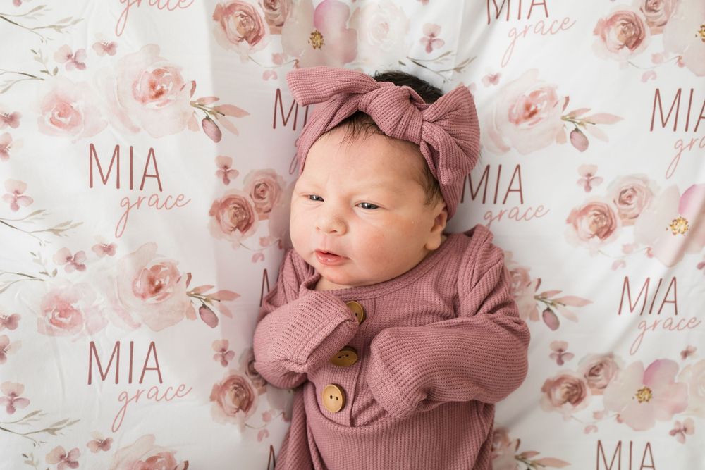 Newborn baby girl named Mia Grace in pink outfit and bow headband on floral personalized name blanket.