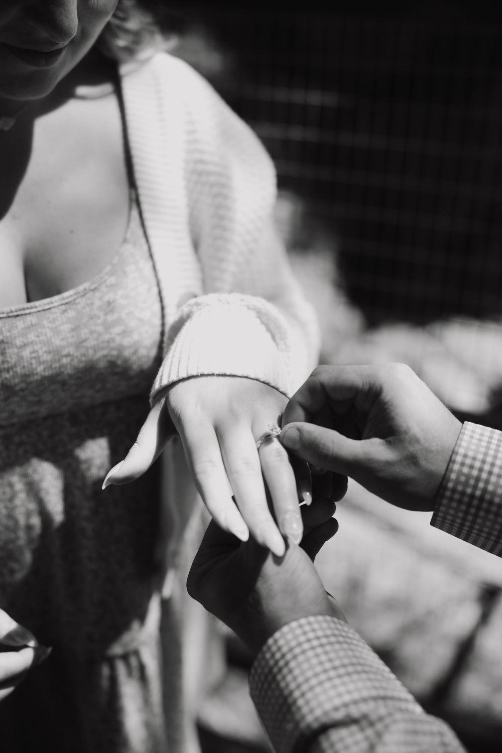 Black and white photo of a man placing an engagement ring on a woman's finger during a romantic proposal.