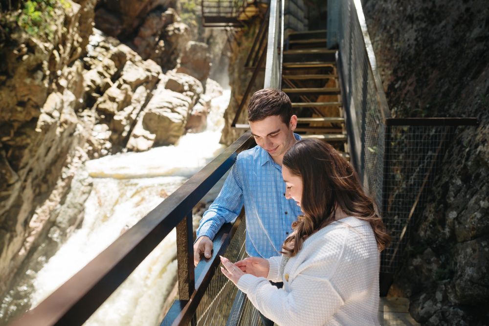 Couple smiling and looking at a phone on a scenic metal staircase beside a rushing waterfall.