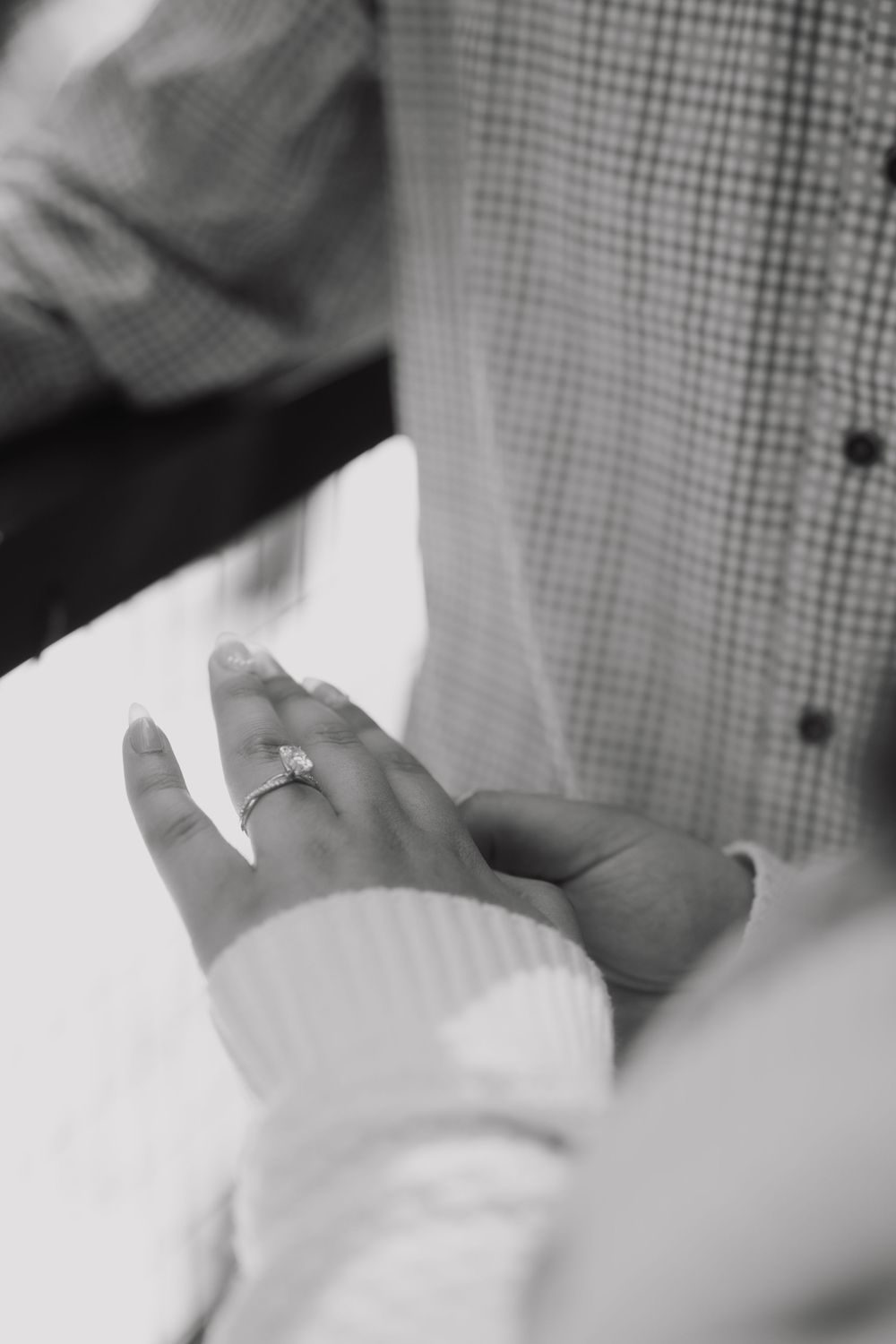 Black and white photo of a couple holding hands, showcasing a diamond engagement ring on the woman's finger.