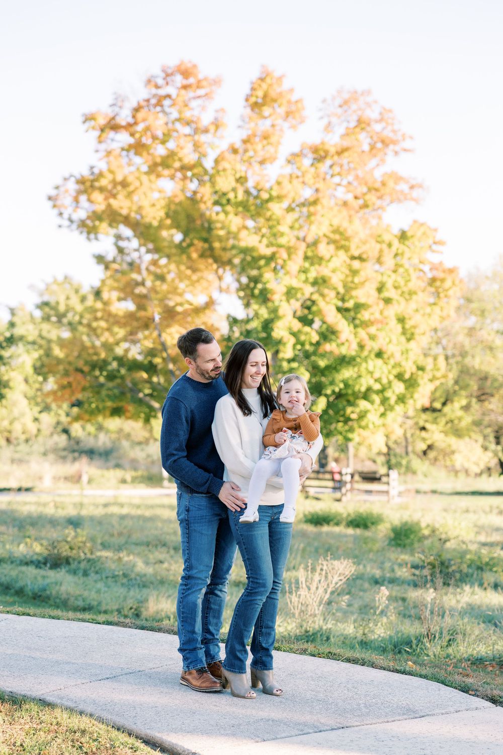 A happy family of three poses on a path surrounded by colorful autumn foliage during a fall outdoor photo session.