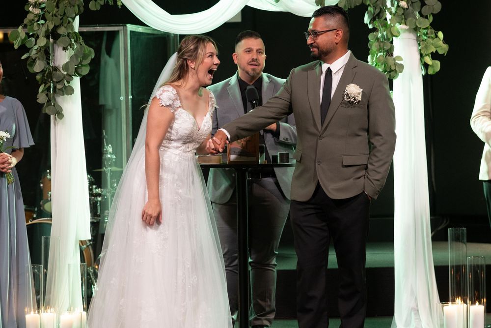 Bride and groom holding hands at wedding ceremony altar with officiant and floral arch backdrop.