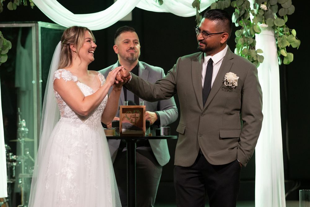 Bride and groom exchanging rings at wedding ceremony with officiant, decorated with greenery arch backdrop.