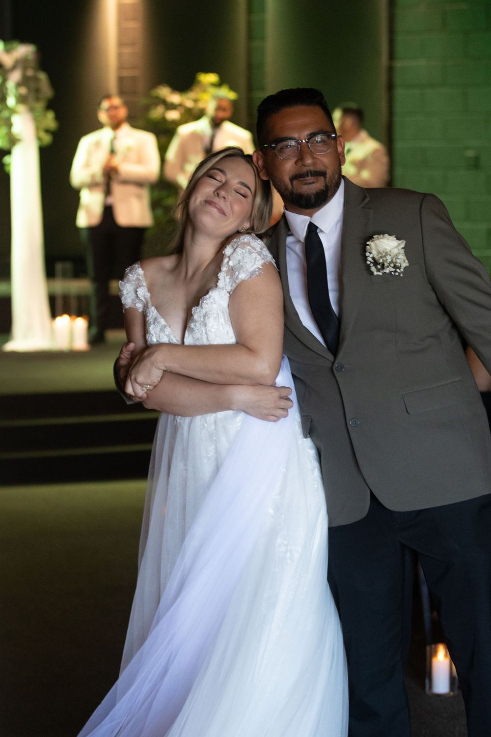 Bride in white lace gown and groom in gray suit with boutonniere share a romantic dance at their wedding reception.