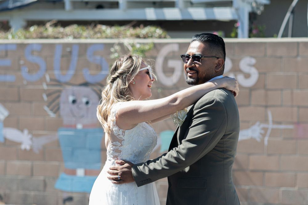 A couple shares a romantic dance outdoors, with the bride in white and groom in a gray suit before a mural.