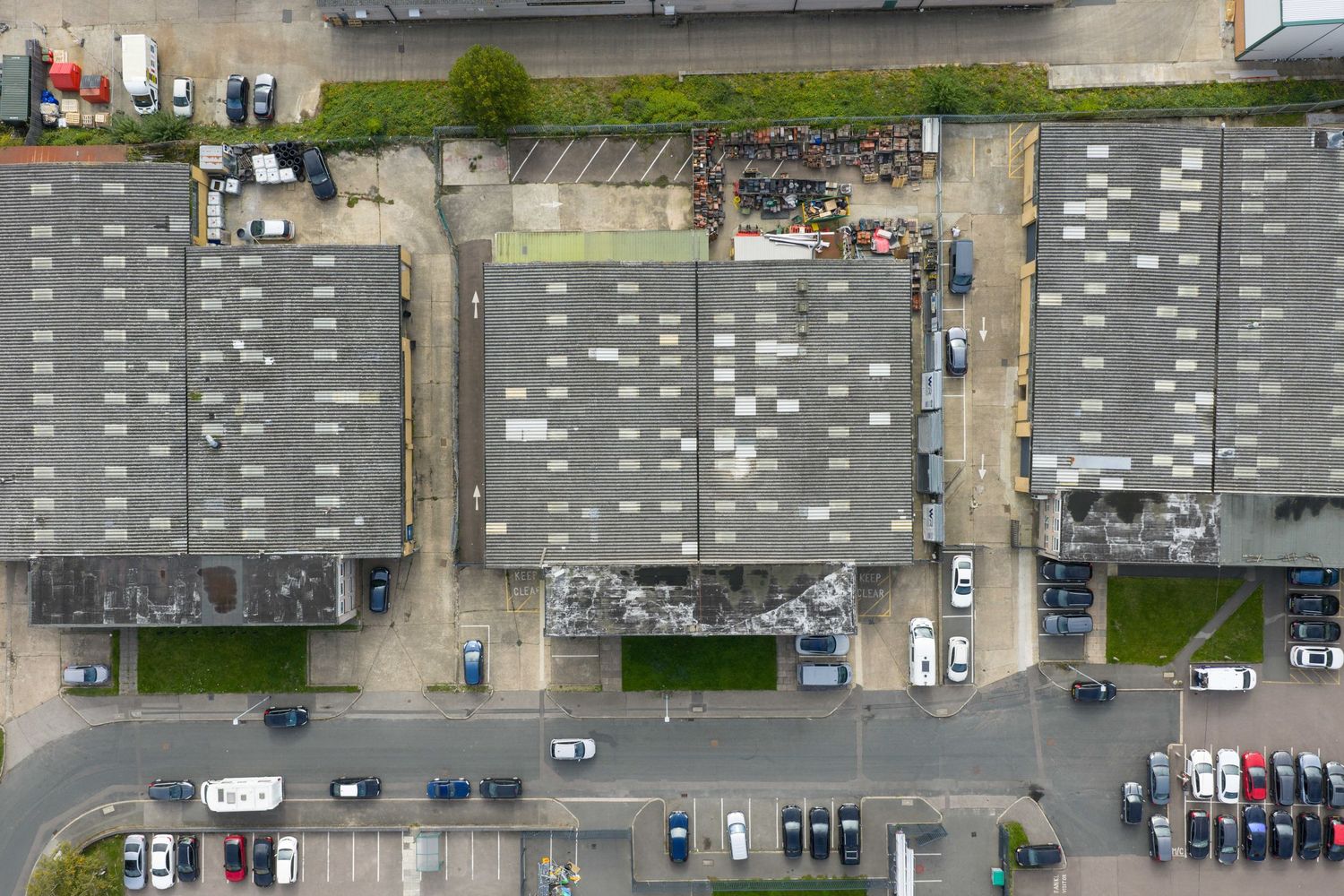 Aerial view of industrial warehouse complex with flat rooftops, parking lots, and surrounding roads in urban area.