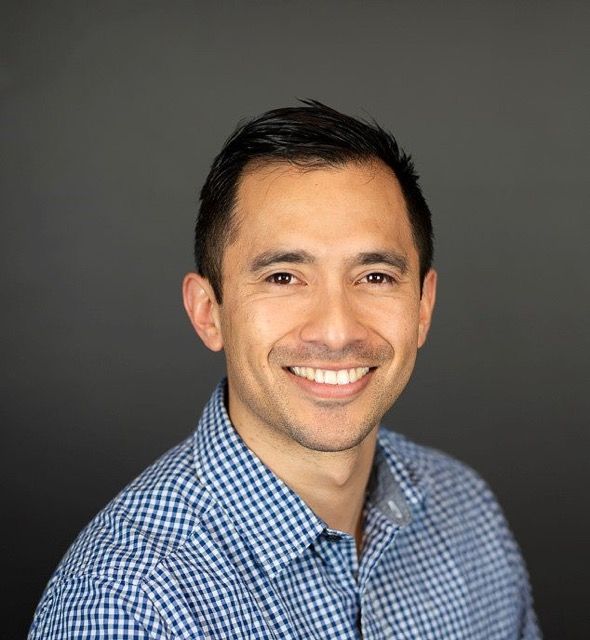 Studio business headshot of a smiling male professional against a dark background