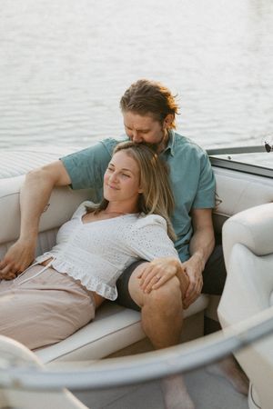 Couple relaxing on a boat, woman leaning back on man as they enjoy a serene moment on the water at golden hour.